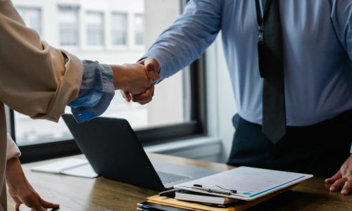 pexels-photo-5673488-5673488 Crop unrecognizable coworkers in formal wear standing at table with laptop and documents while greeting each other before meeting